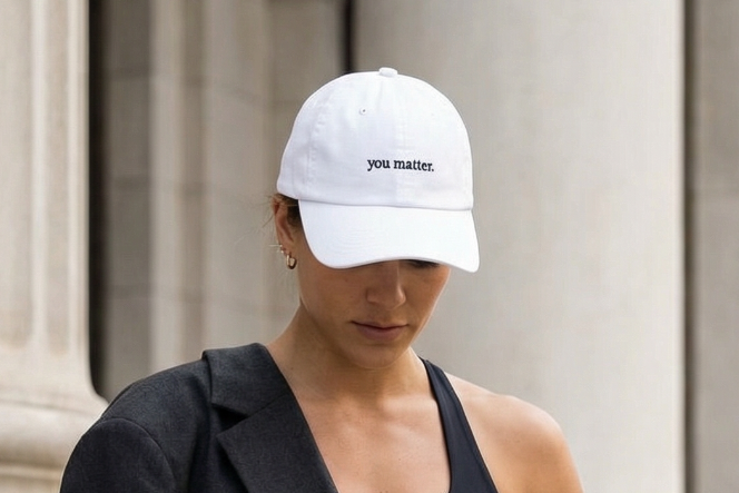 Person wearing a black outfit with a white cap, standing in front of classical architecture.